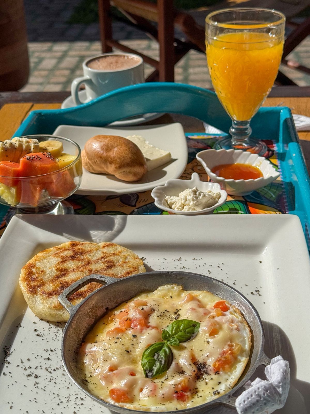A breakfast tray with a grilled English muffin, a bowl of scrambled eggs with tomatoes and cheese, a glass of orange juice, and a cup of coffee.