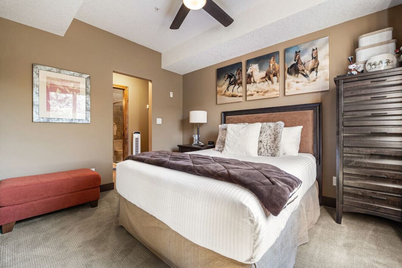 Habitación de hotel con cama, banca, cómoda y ventilador de techo.