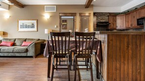 A cozy living room with a wooden dining table and chairs, a sofa, and a kitchen area with wooden cabinets and a stone backsplash. - Wild Horses | Pool | Hot Tub | Hot Springs (Radium Hot Springs)