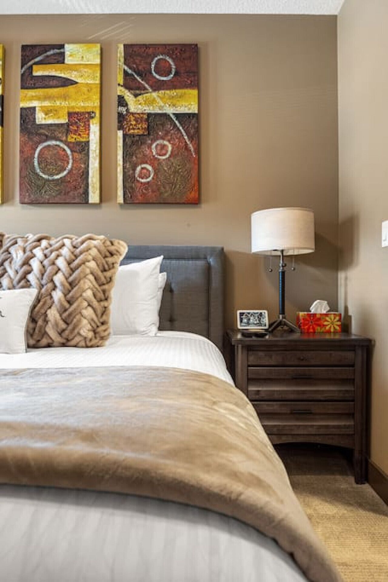 A bedroom with a bed, a nightstand, a lamp, and abstract wall art.