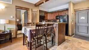 A dining area with a table set for four, wooden chairs, and a kitchen with wooden cabinets and a refrigerator. - Wild Horses | Pool | Hot Tub | Hot Springs (Radium Hot Springs)