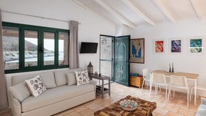 Una sala de estar con un sofá, una mesa de centro, una mesa de comedor con sillas, un televisor montado en la pared y una puerta que da al exterior.