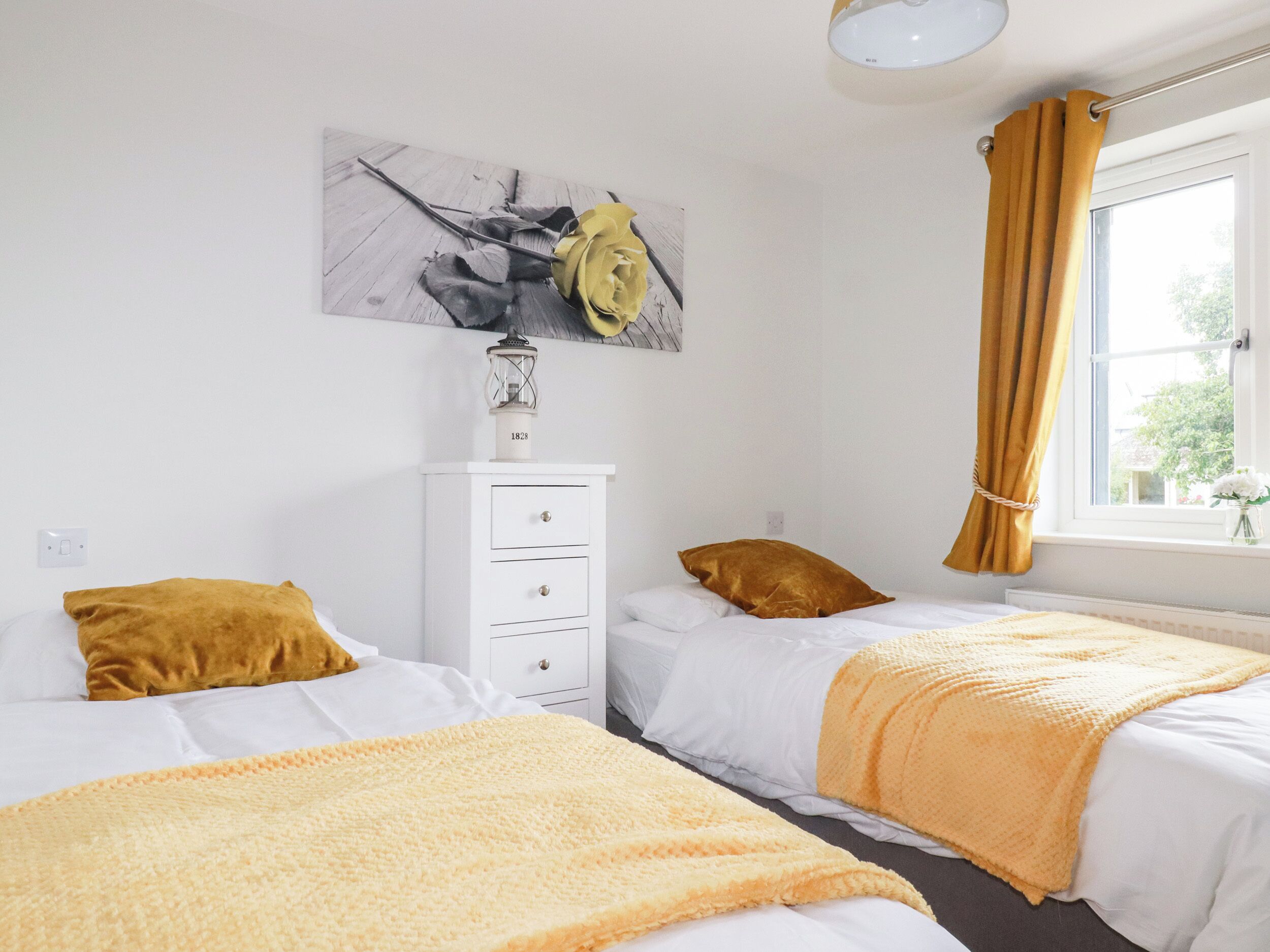 A bedroom with two beds, a white dresser, a lamp, and a window with curtains.