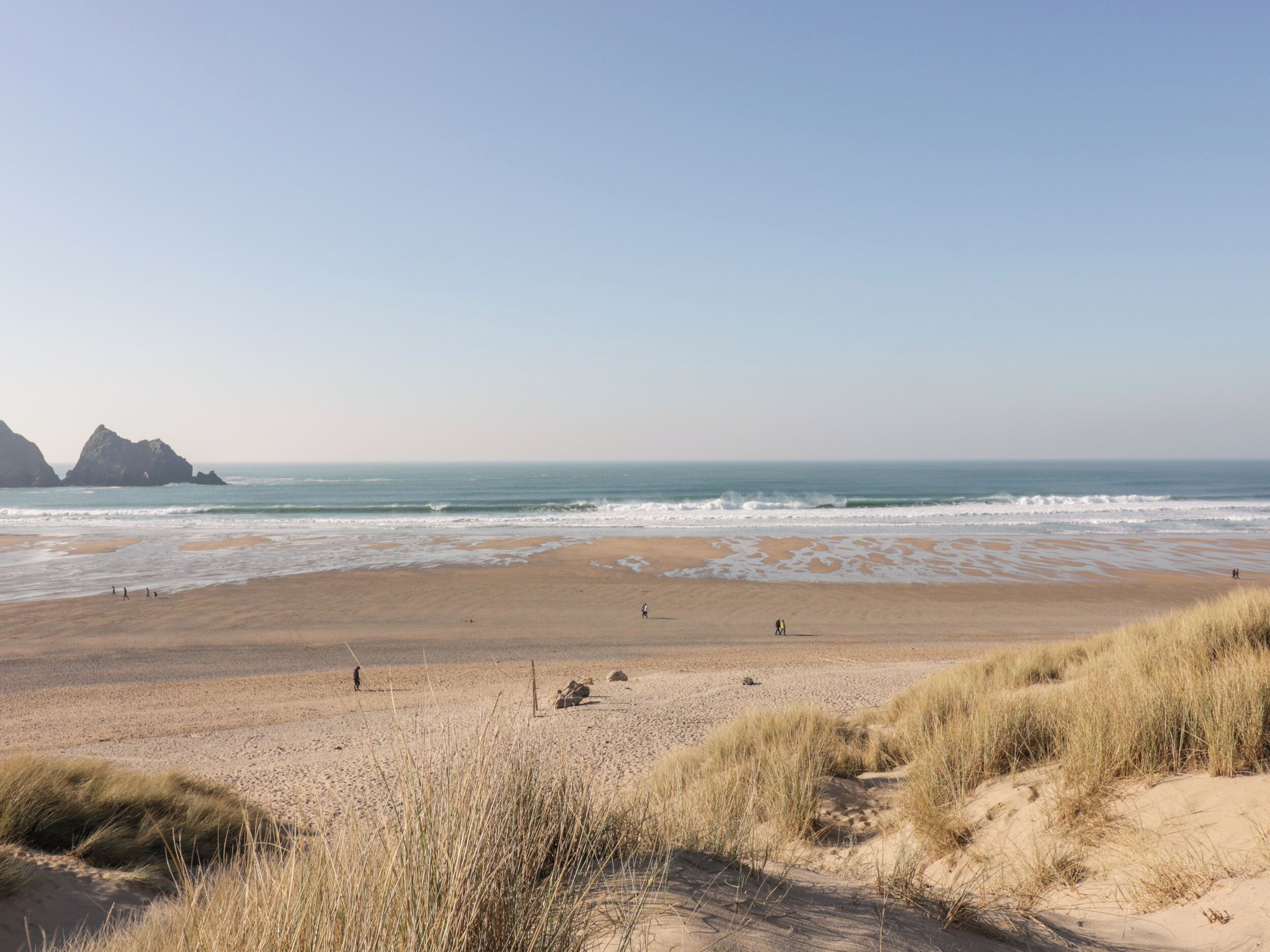 A beach with sand dunes and rocky outcrops in the distance.