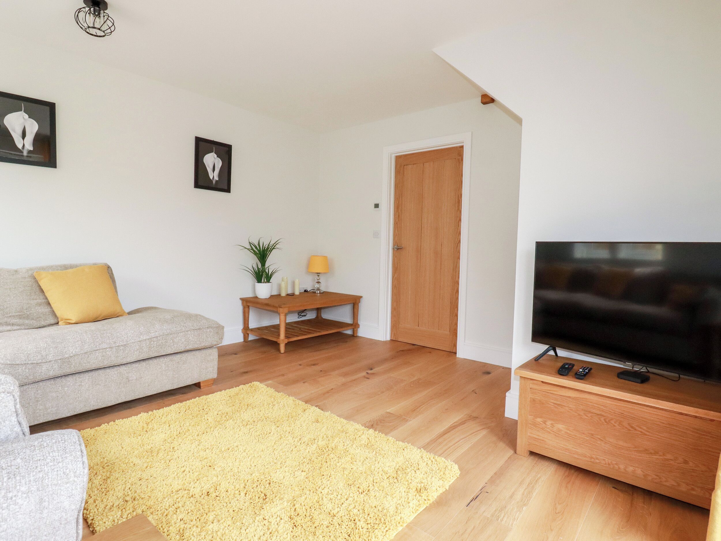 Een woonkamer met een grijze bank, een geel kussen, een houten tv-meubel en een geel vloerkleed.