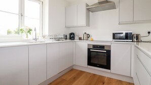 A modern kitchen with white cabinets, a stainless steel range hood, a built-in oven, a microwave, and a coffee maker. - Chynoweth House (Newquay)