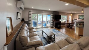 A spacious living area with a sofa, a coffee table, and a TV. There is a sliding glass door leading to a balcony with a view of a body of water. - Lake Front Retreat with Deep Water Dock (Weare)