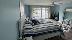 A bedroom with a bed, a desk, a chair, a large window, and a view of a body of water. - Lake Front Retreat with Deep Water Dock (Weare)