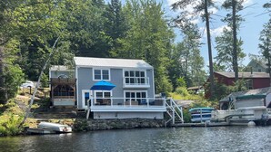 A house with a dock extending into a body of water, surrounded by trees and other buildings. - Lake Front Retreat with Deep Water Dock (Weare)