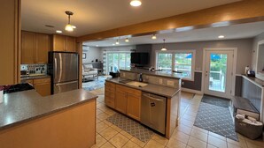 A spacious kitchen with a large island, stainless steel appliances, and a view of the backyard through large windows. - Lake Front Retreat with Deep Water Dock (Weare)