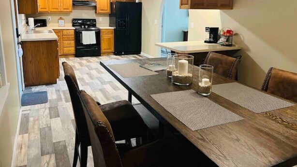 Une cuisine moderne avec des meubles en bois, un réfrigérateur noir et un coin repas comprenant une table et des chaises en bois.