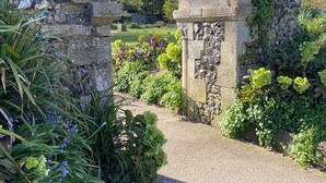 Un arc de pedra amb vegetació, que condueix a un camí envoltat de plantes i flors.