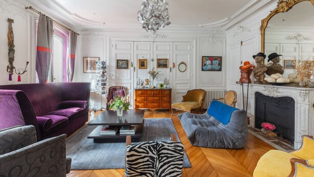 A spacious living room with a purple sofa, a grey armchair, a blue bean bag, and a wooden coffee table. A fireplace with a mirror and decorative items is visible in the background. - Sophisticated and Grand Apt. in Perfect Location! (Paris)