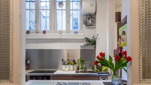 A kitchen with a window, a water heater, and a vase with red flowers. - Sophisticated and Grand Apt. in Perfect Location! (Paris)