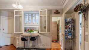 A dining area with a table and two chairs, a radiator, and a window with shutters. - Sophisticated and Grand Apt. in Perfect Location! (Paris)