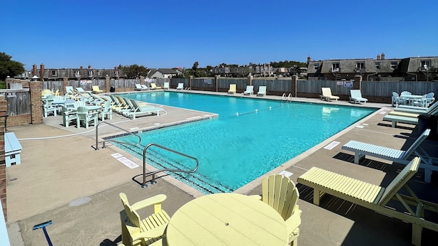 A rooftop pool with multiple lounge chairs and a table, surrounded by buildings. - Stylish Coastal Retreat in the Heart of the OBX 
2BR•2BA•Pool•Tennis•Patio•WiFi (Kitty Hawk)