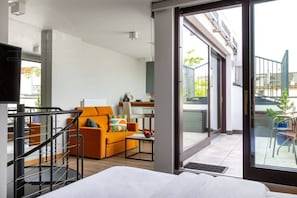 Una camera d'albergo moderna con un balcone, un divano, un tavolo da pranzo e una TV.