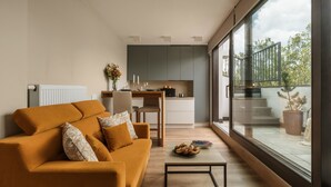A modern living room with a sofa, a coffee table, and a view of a kitchen and balcony. - ArtSquare by Fragola Apartments (Kraków)