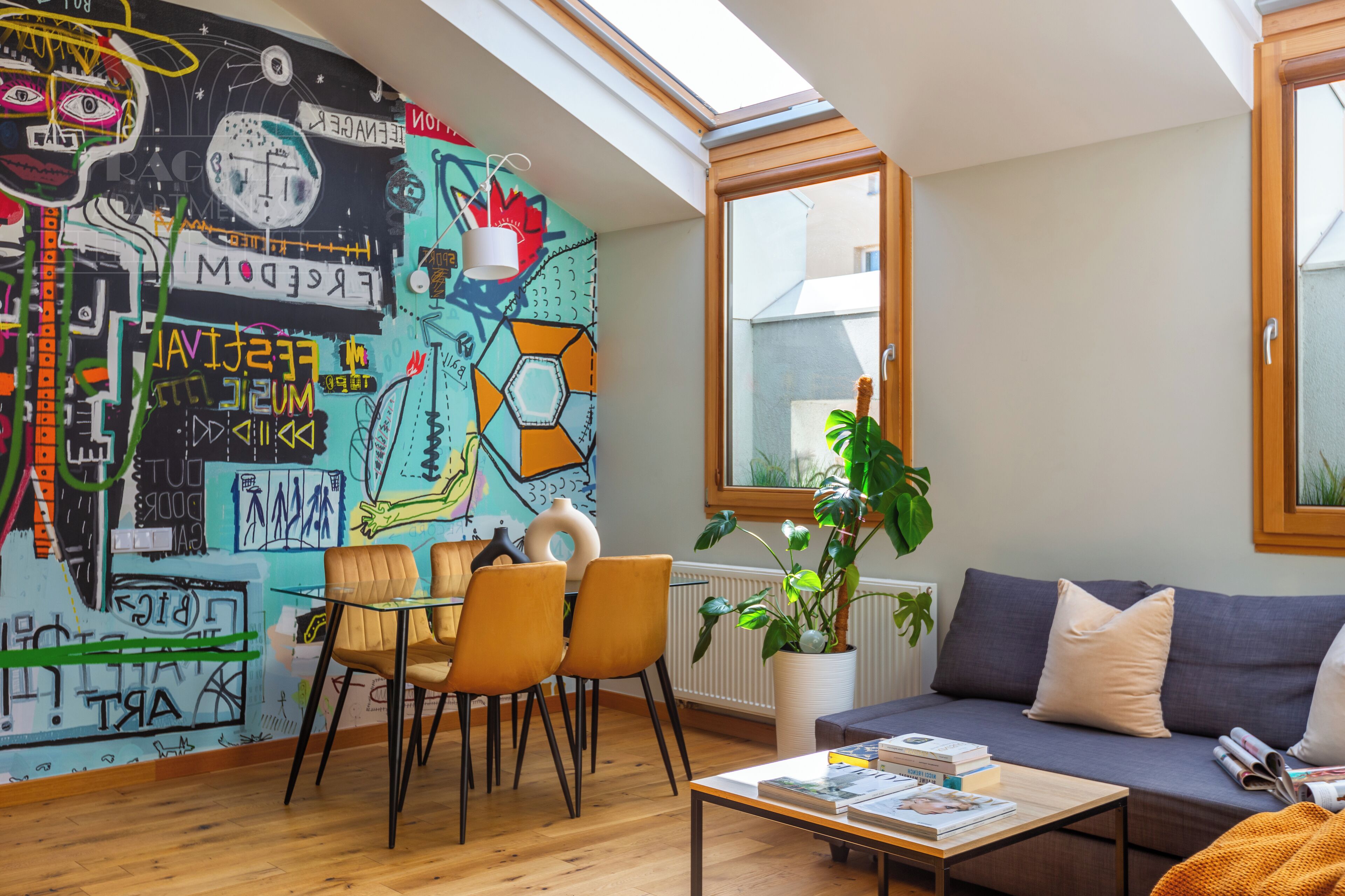 A modern living room with a colorful mural, a dining area with chairs, a sofa, and a coffee table with books.