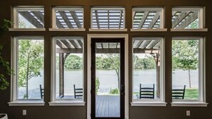 Une pièce dotée d’une grande fenêtre donnant sur un plan d’eau, d’une terrasse en bois et d’une porte menant à l’extérieur.
