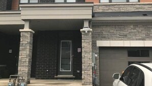 A two-story building with a covered front porch, a garage, and a parked white car. - Niagara Relaxing Getaway - La Maison de Niagara (Niagara Falls)