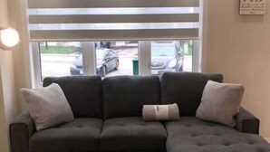 A sectional sofa with a patterned rug in a living room with a window and blinds. - Niagara Relaxing Getaway - La Maison de Niagara (Niagara Falls)