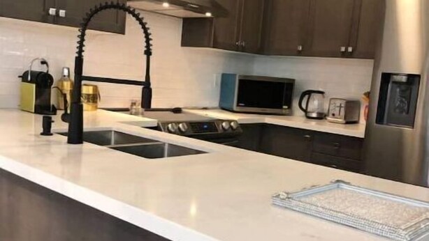 A modern kitchen with dark wooden cabinets, a white countertop, a stainless steel refrigerator, and a black faucet. - Niagara Relaxing Getaway - La Maison de Niagara (Niagara Falls)