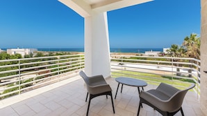 Un balcon avec deux chaises et une table, offrant une vue sur la côte, avec des bâtiments et de la végétation.