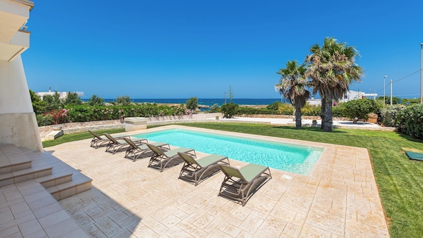 Une piscine avec des chaises longues, une vue sur la mer et une pelouse bien entretenue.
