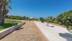 Un chemin pavé, bordé d’un côté par un muret en pierre et de l’autre par une zone herbeuse, qui mène à une étendue d’eau.