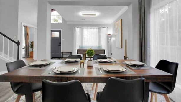 A modern dining area with a wooden table set for six, black chairs, and a view of the kitchen in the background. - Luxury & Bright ~ 2 Master BR ~ Games ~ Backyard! (Houston)