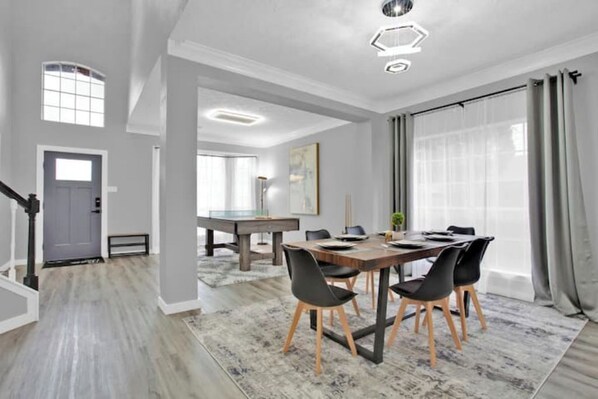 Un comedor moderno con una mesa de madera y sillas negras, un ventanal con cortinas y una escalera que lleva a otra habitación.