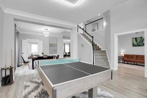 Amplia sala de estar con mesa de ping-pong, una escalera y un rincón de descanso acogedor.