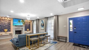 A modern living room with a sofa, a coffee table, and a fireplace. There is a blue door and a stone wall with a painting. - Luxury Home 4 Rooms ~ Pool Table & Poker~ King Bed (Houston)