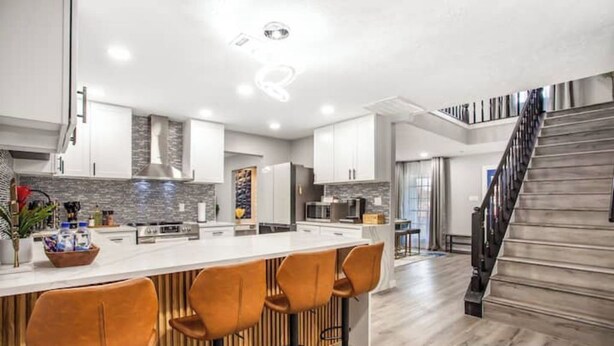 A modern kitchen with a central island, wooden bar stools, and a staircase leading to another level. - Luxury Home 4 Rooms ~ Pool Table & Poker~ King Bed (Houston)