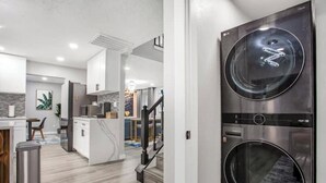 A modern kitchen with white cabinets, a stainless steel trash bin, and a staircase leading to another level. - Luxury Home 4 Rooms ~ Pool Table & Poker~ King Bed (Houston)