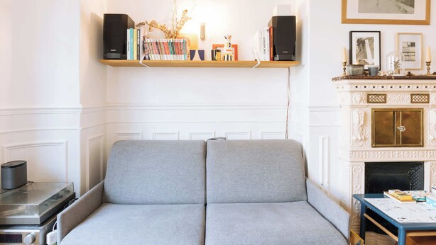 A room with a grey sofa, a wooden shelf with books, a fireplace, and a framed picture on the wall. - Central, Spacious Family Apartment with Balcony (Paris)