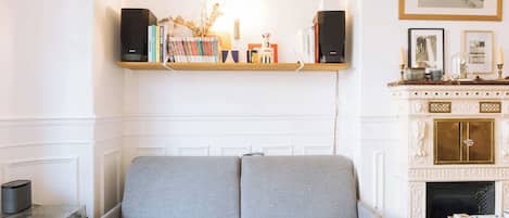 Una habitación con un sofá gris, una estantería de madera con libros, una chimenea y un cuadro en la pared.