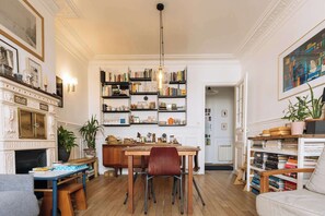 A room with a fireplace, wooden dining table, chairs, bookshelves, and a variety of decorative items. - Central, Spacious Family Apartment with Balcony (Paris)