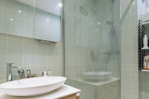 A modern bathroom with a glass-enclosed shower, a white sink, and a mirror above the sink. - Central, Spacious Family Apartment with Balcony (Paris)