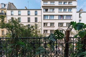 A multi-story residential building with balconies, a wrought iron fence, and lush greenery.