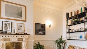 A room with a fireplace, framed pictures, a bookshelf, and potted plants. - Central, Spacious Family Apartment with Balcony (Paris)