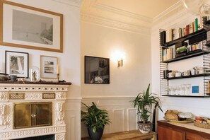 A room with a fireplace, framed pictures, a bookshelf, and potted plants. - Central, Spacious Family Apartment with Balcony (Paris)