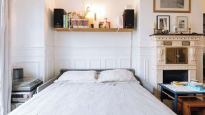 A bedroom with a bed, a fireplace, a shelf with books, and a framed picture on the wall. - Central, Spacious Family Apartment with Balcony (Paris)