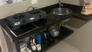 Une cuisine équipée d’une cuisinière à gaz, d’un évier, d’un mixeur et d’une étagère où sont rangées des tasses et une casserole.