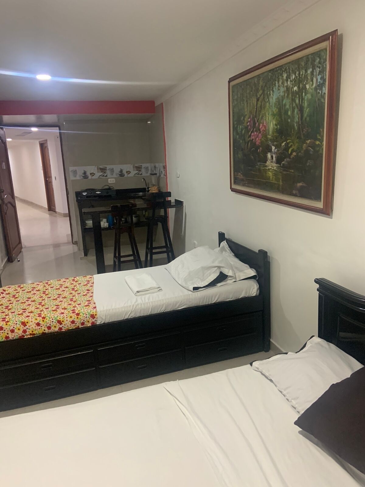 Une chambre à coucher avec un lit, un bureau et une chaise. Il y a un tableau accroché au mur.