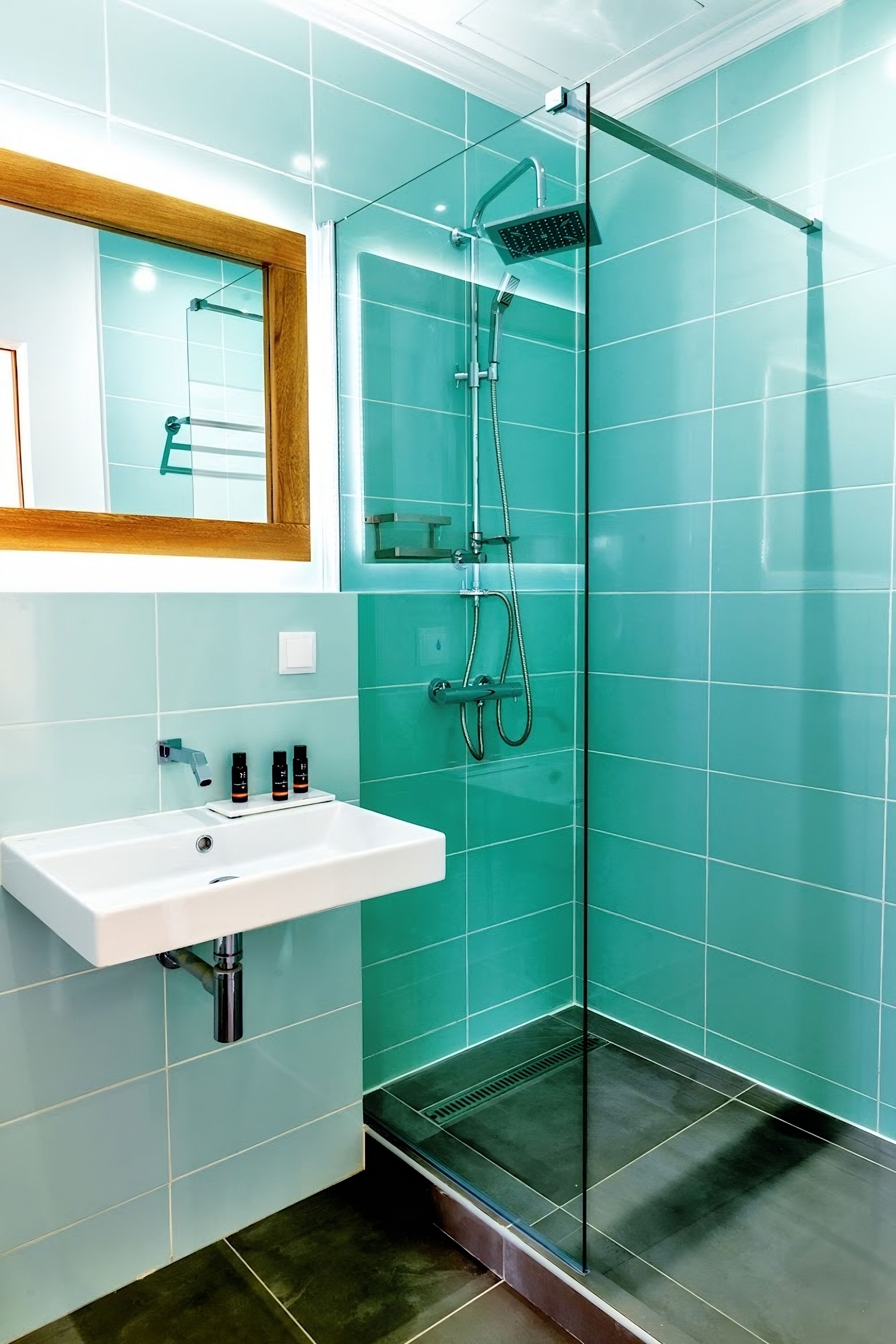 Uma casa de banho moderna com chuveiro em cabine de vidro, lavatório branco e azulejos azul-turquesa.