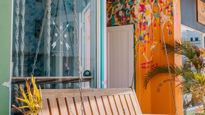 En gungstol i trä med kuddar, ett fönster med en gardin av rep och en färgglad vägg med en skylt som lyder: ”Art Hotel Bonaire”.