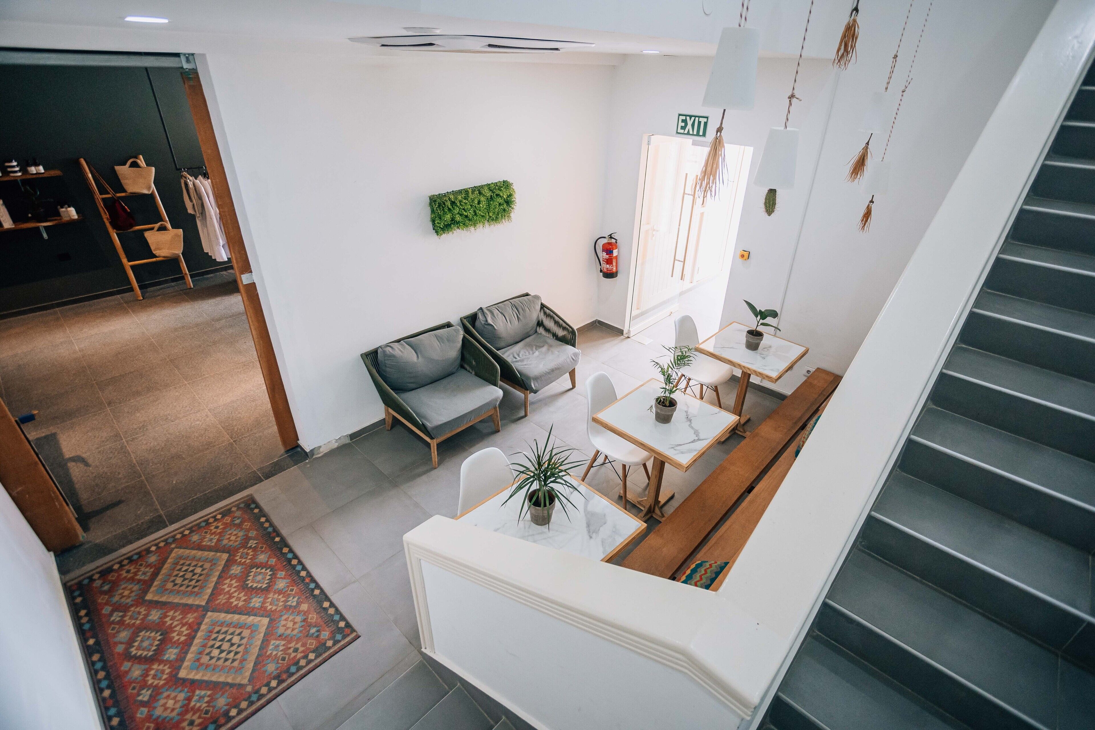A modern interior with a staircase, a reception area with a sofa and chairs, a small table with a plant, and a fire extinguisher on the wall.