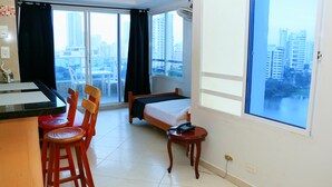 A hotel room with a bed, a small table with a phone, a chair, a desk with a chair, and a large window offering a city view. - Apartment 1c11 Near The Sea With Pool (Cartagena)